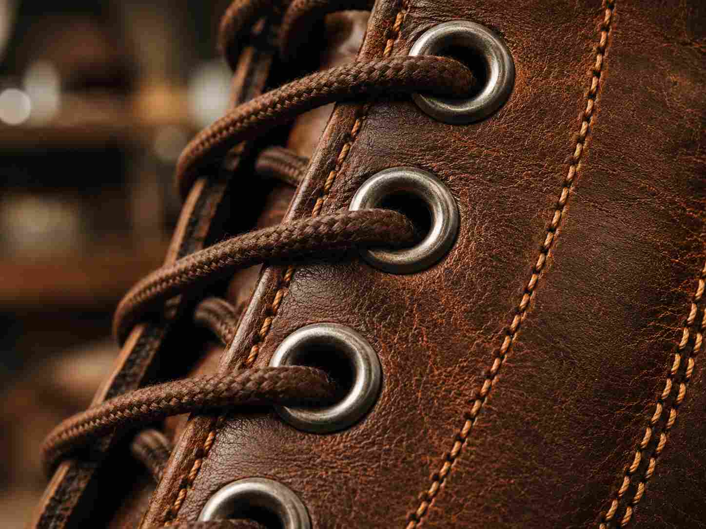custom eyelets, Dark custom eyelets with brown laces are shown in close-up on a stitched leather boot.